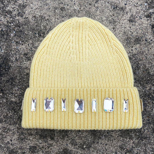 light yellow beanie with gemstone decorations on a textured gray background
