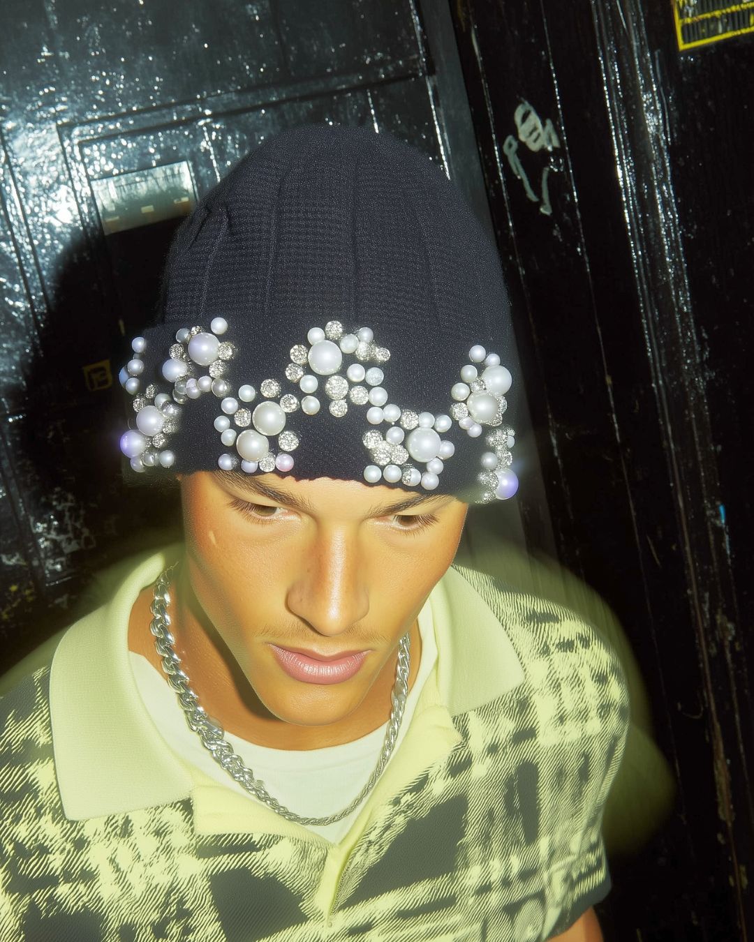 Person wearing a black knit beanie with decorative elements against a dark background