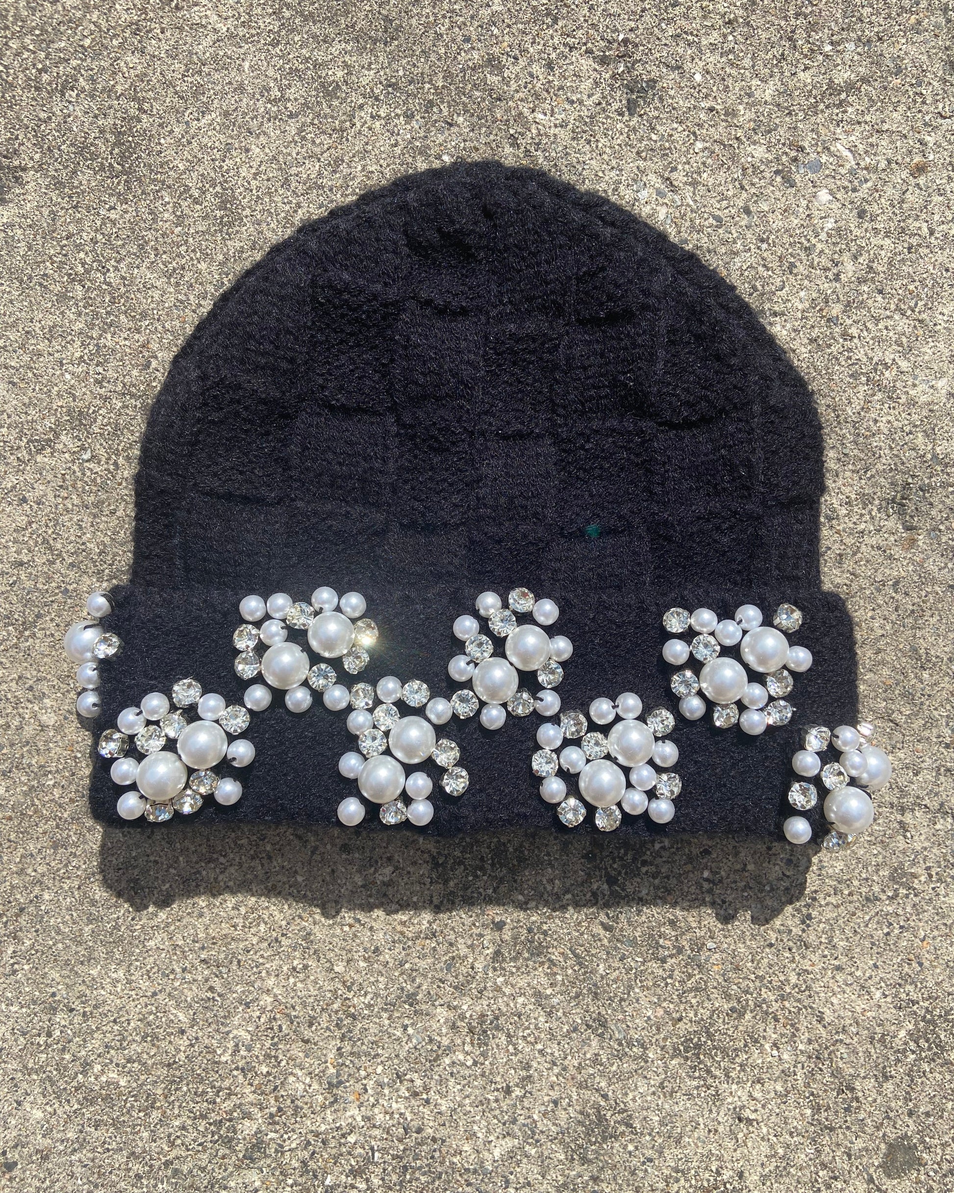 Black knit beanie with decorative pearls and crystals in a glittering checkerboard pattern on a concrete surface