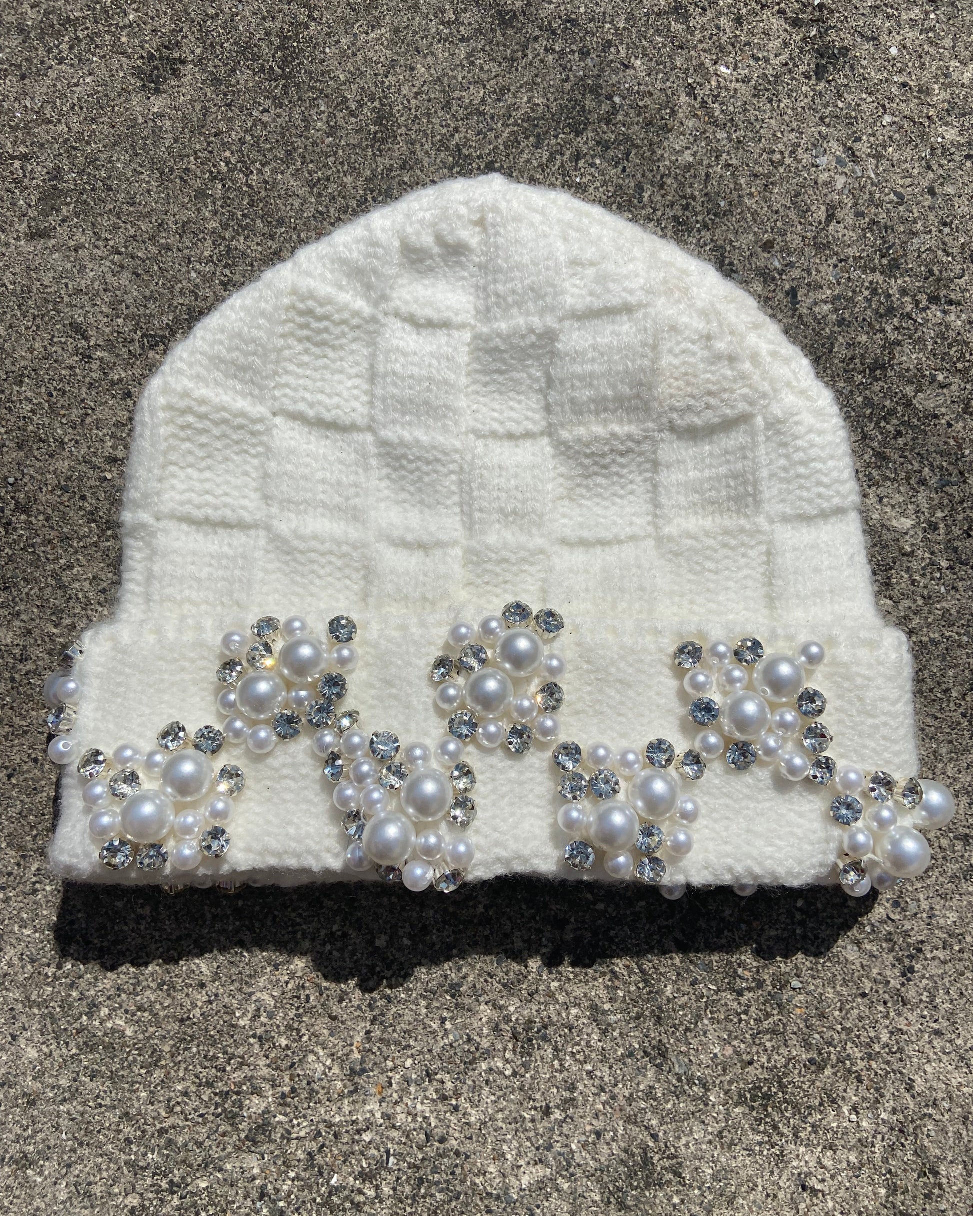 White knitted headband with decorative pearls and crystals on a textured surface